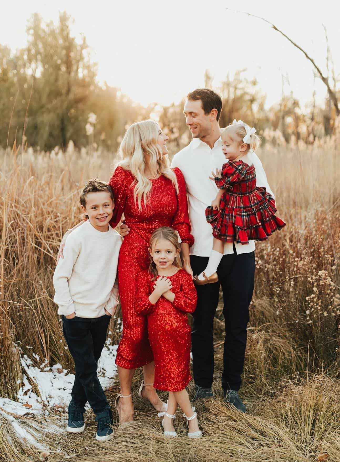 A Christmas family photo with a family of five with the girls wearing sparkly red and red plaid dresses and the boys wearing black pants and white tops