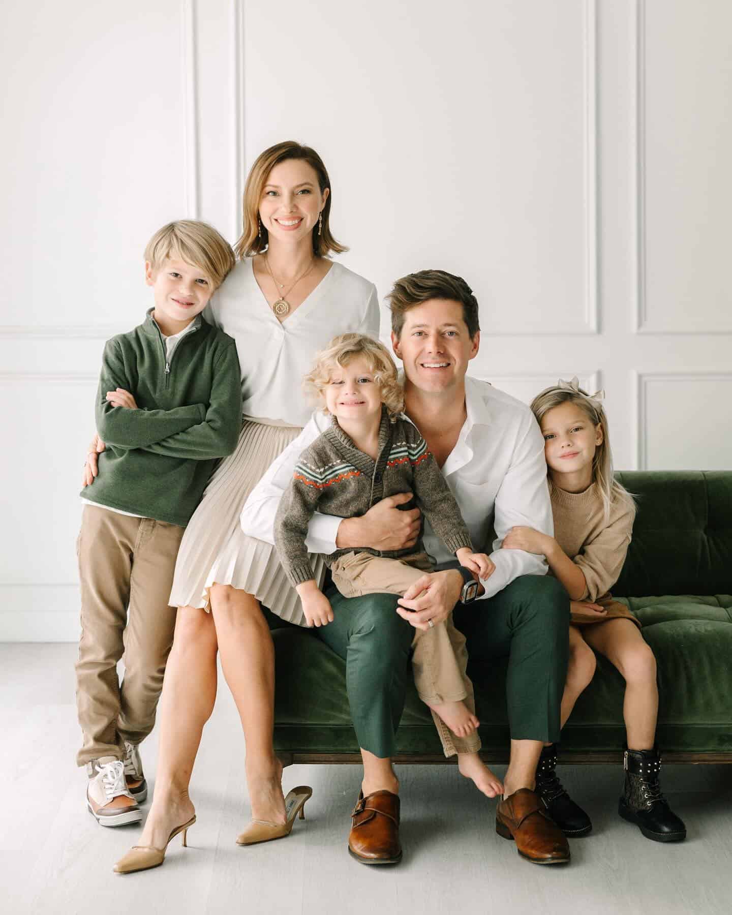 Family photos with a family of five, wearing shades of green, beige, and white while sitting on a green couch