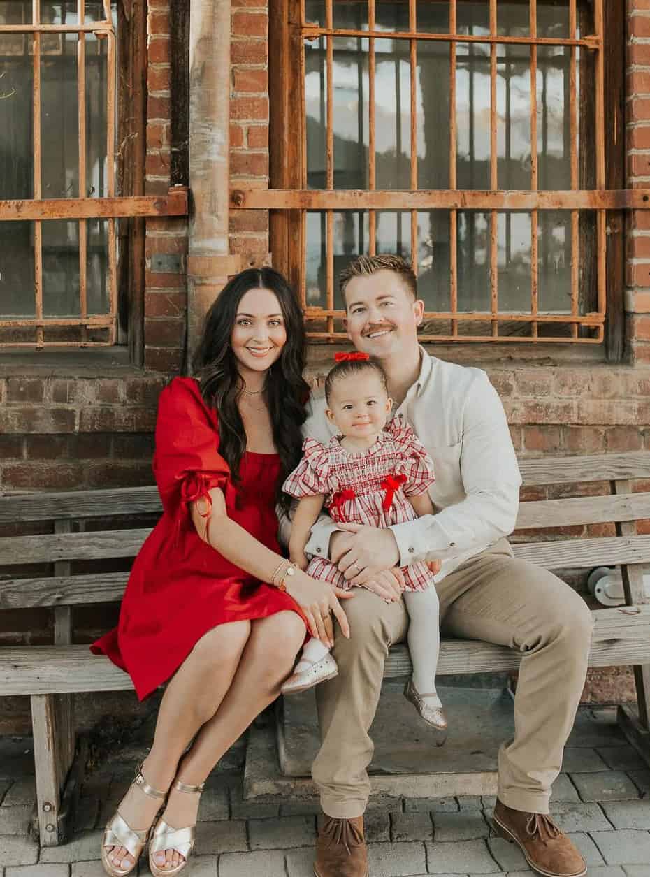 A family photo with a family of three wearing white, beige, and red pieces