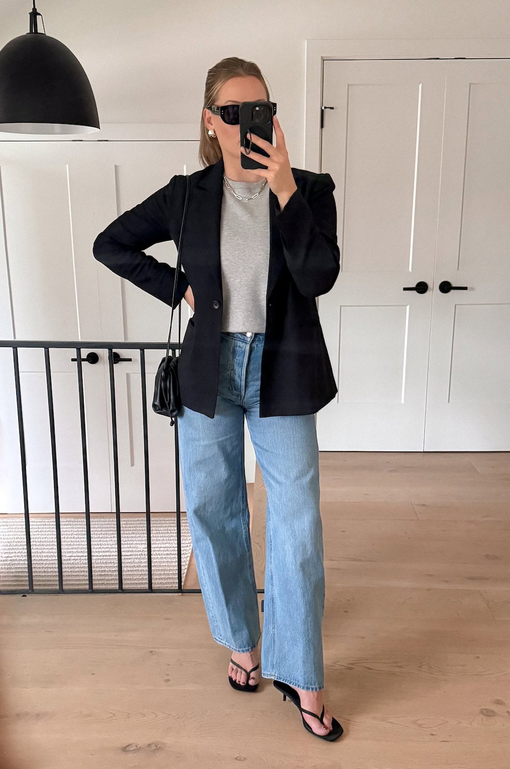 Christal wearing light wash wide leg jeans, a grey sweater and a black blazer.