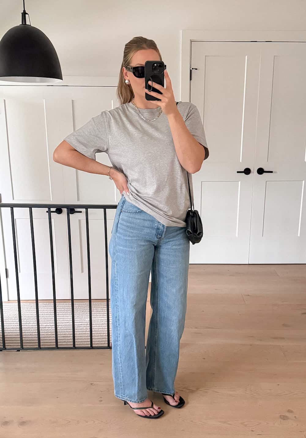 Christal wearing light wash wide leg jeans with a grey t-shirt and black heeled sandals.