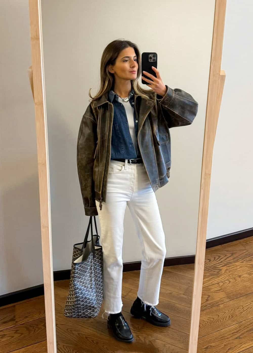 Woman wearing white jeans with black loafers and a leather jacket.