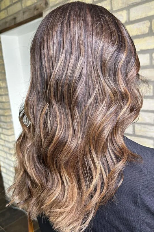 Woman with dark brunette hair and caramel balayage.