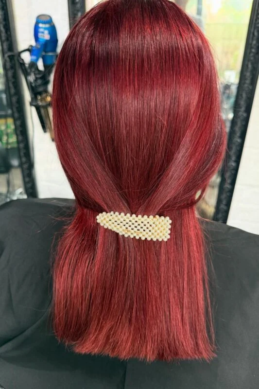 Woman with straight crimson red hair accented with a pearl barrette.