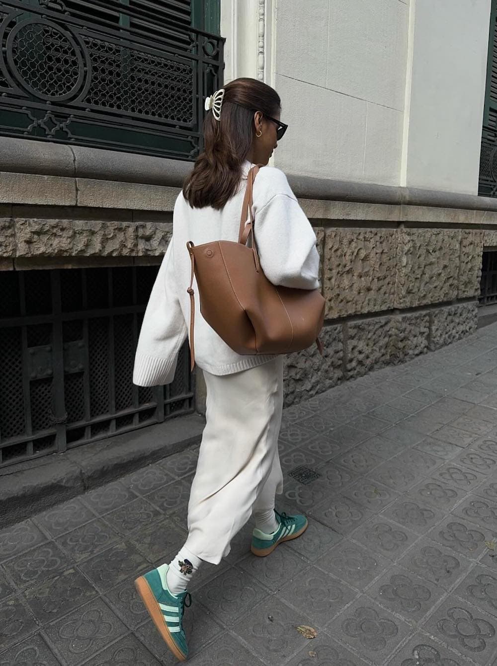 Woman wearing a white maxi skirt with a white sweater and sneakers.