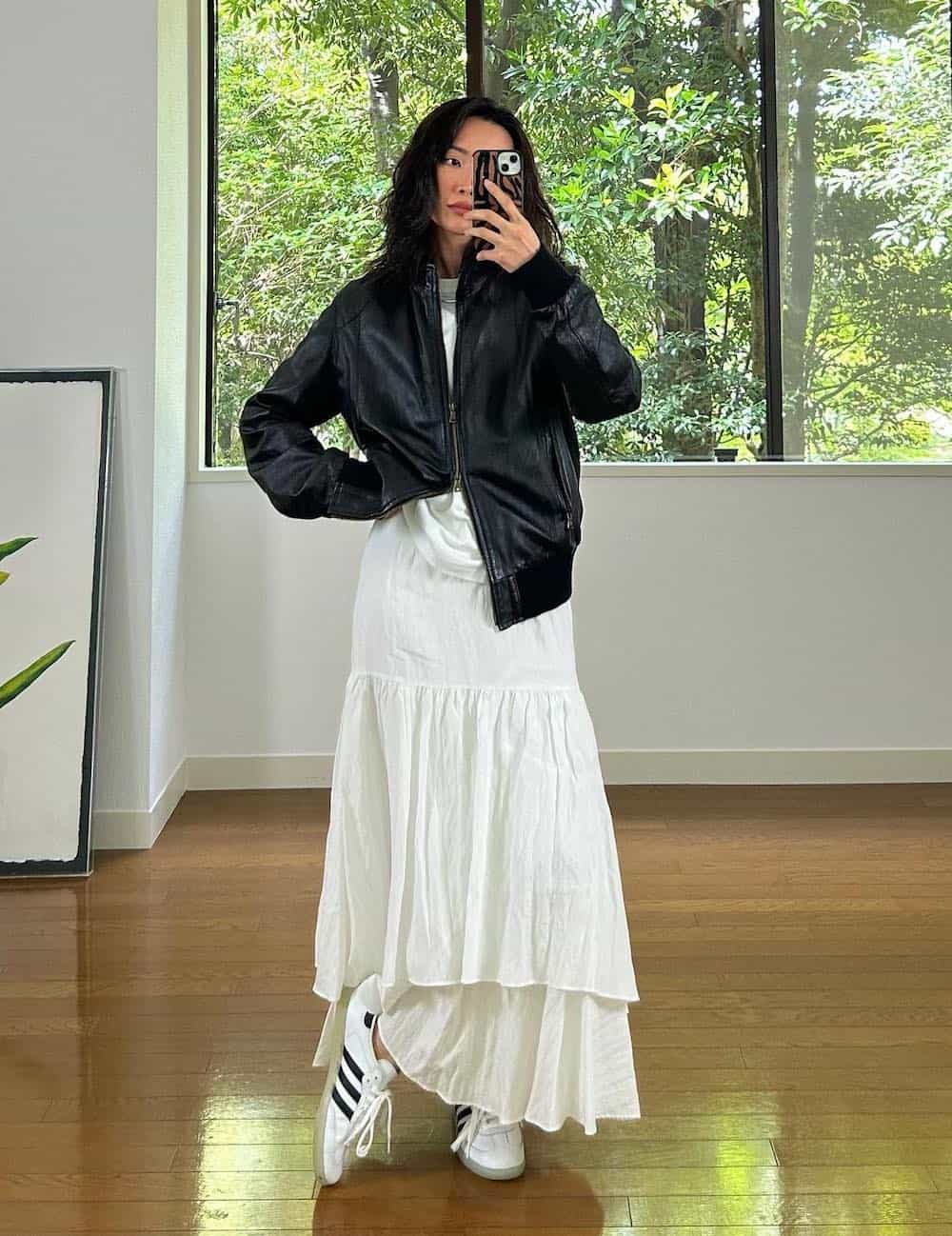 Woman wearing a white silk maxi skirt with sneakers and a black jacket.