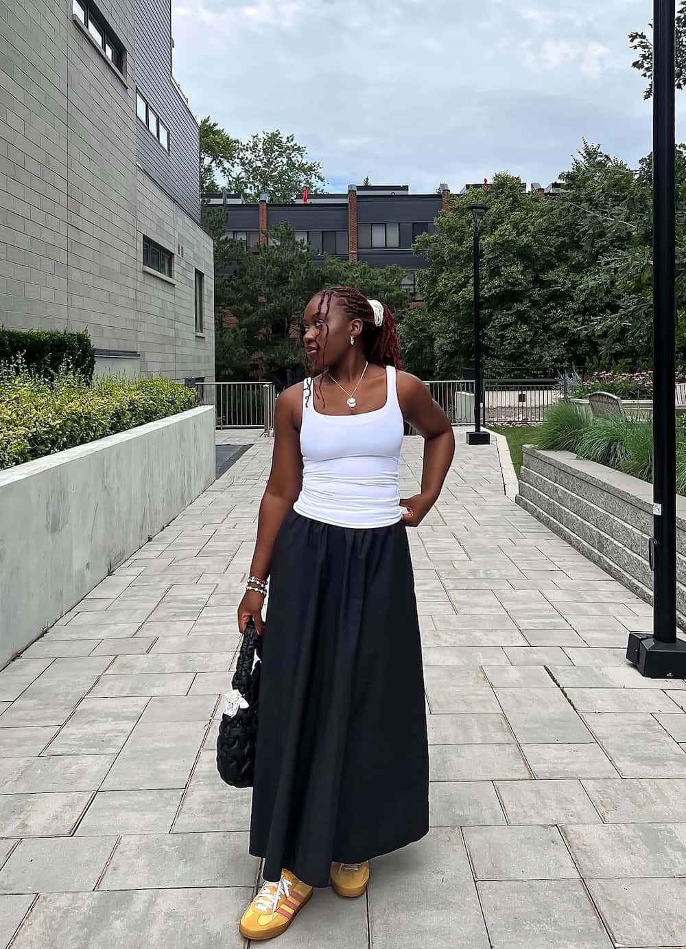 Woman wearing a black maxi skirt with a whit tank top and sneakers.