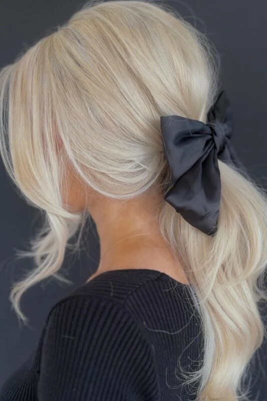 Woman with a messy low ponytail featuring side bangs and a black satin bow.