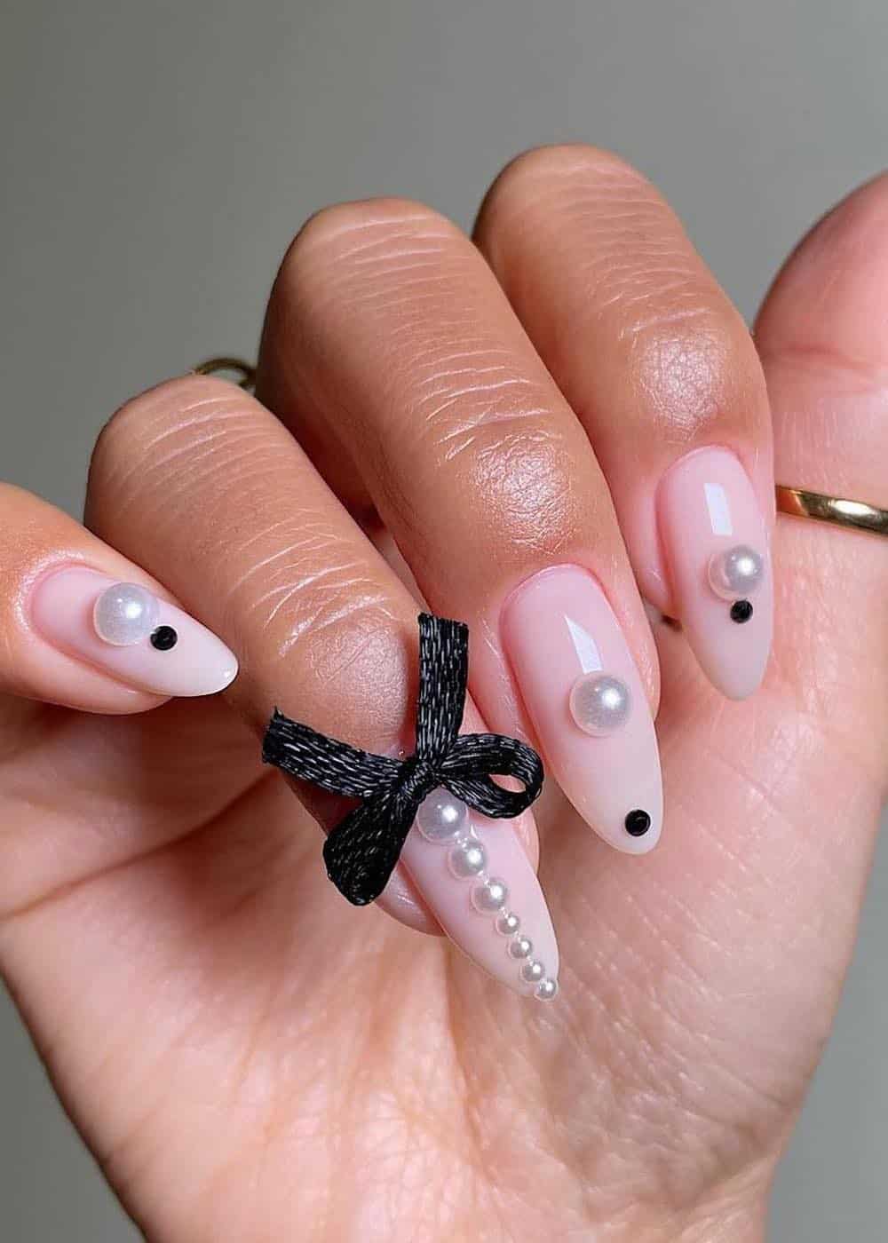 long nude pink pointy nails with pearls, black gems, and black bows