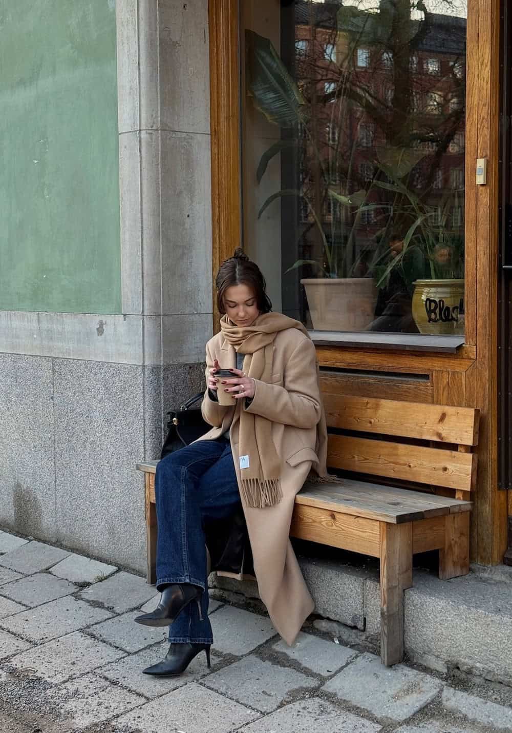 Woman wearing dark jeans with a tan coat and scarf.