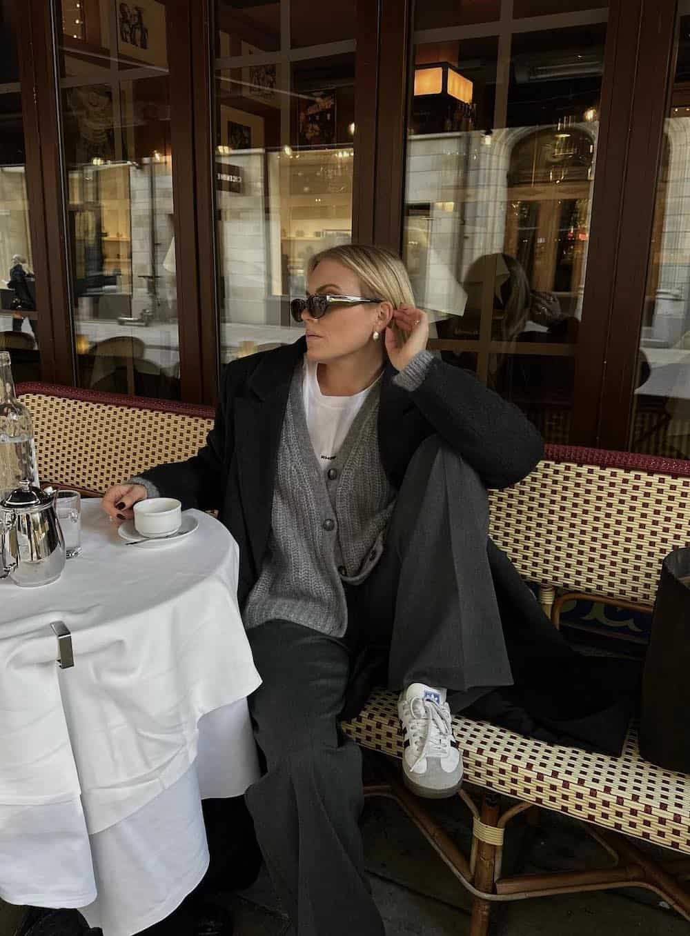 Woman wearing black pants with an oversized sweater over a white tee and sneakers.