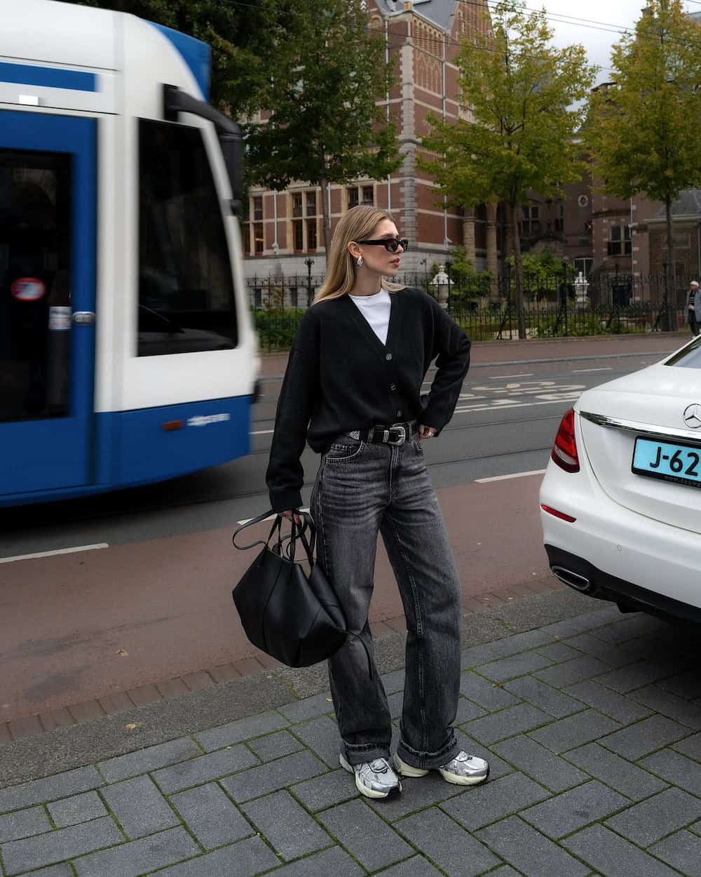 Woman wearing black wide leg jeans with athletic sneakers and a cardigan.