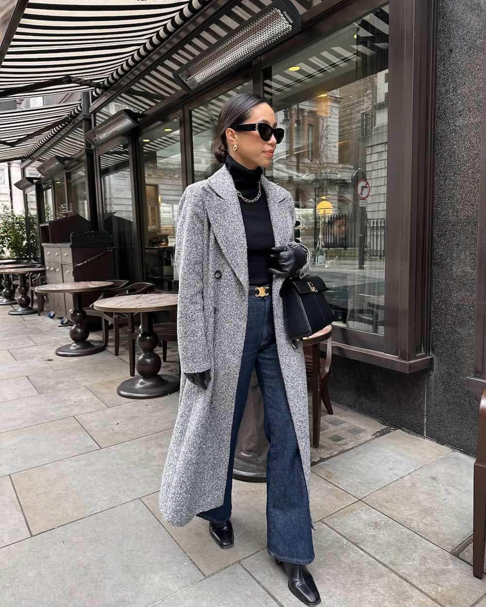 Woman wearing dark wash wide leg jeans with a black turtleneck and a grey duster coat.