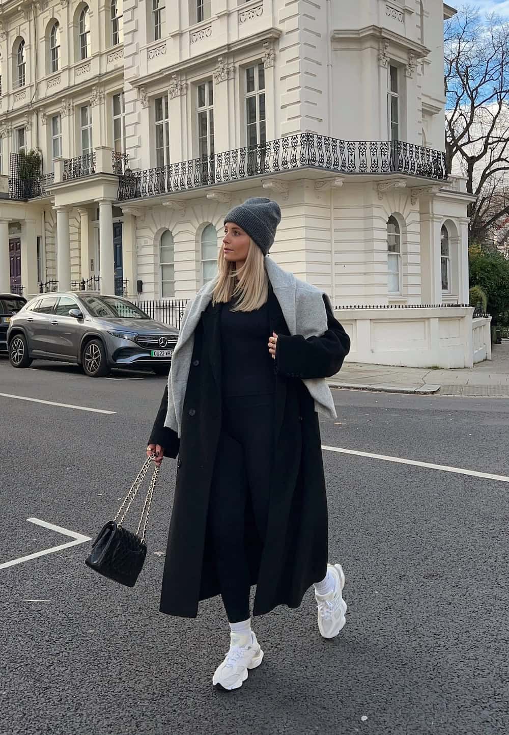 Woman wearing a long coat with leggings and sneakers.