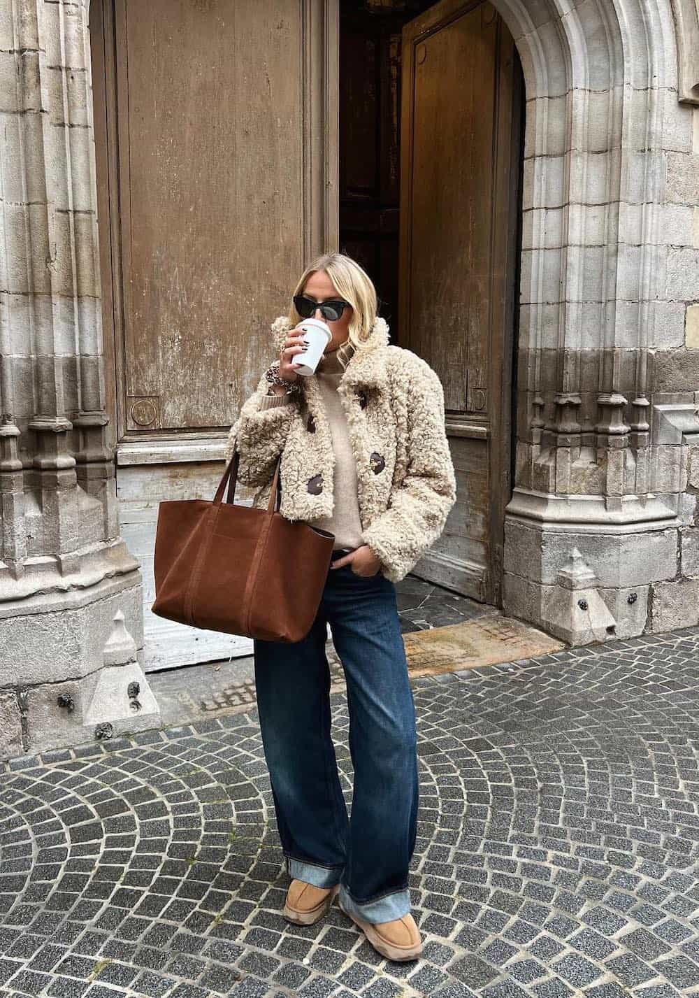 Woman wearing baggy jeans, a sweater and a sherpa jacket with Ugg boots.